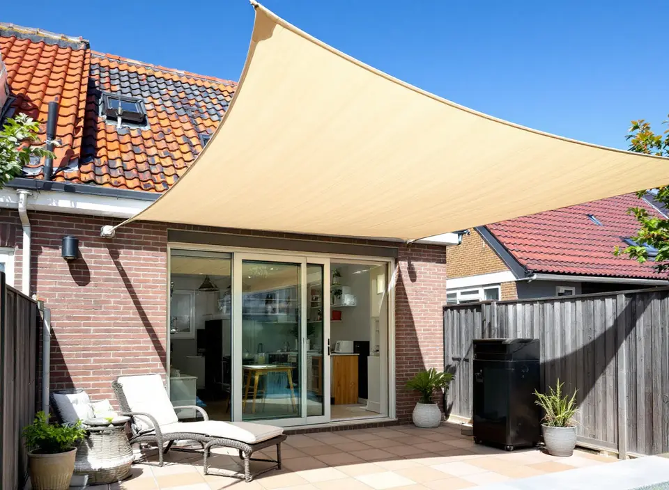 Zandkleurig schaduwdoek gespannen boven het terras van een bakstenen huis met pannendak